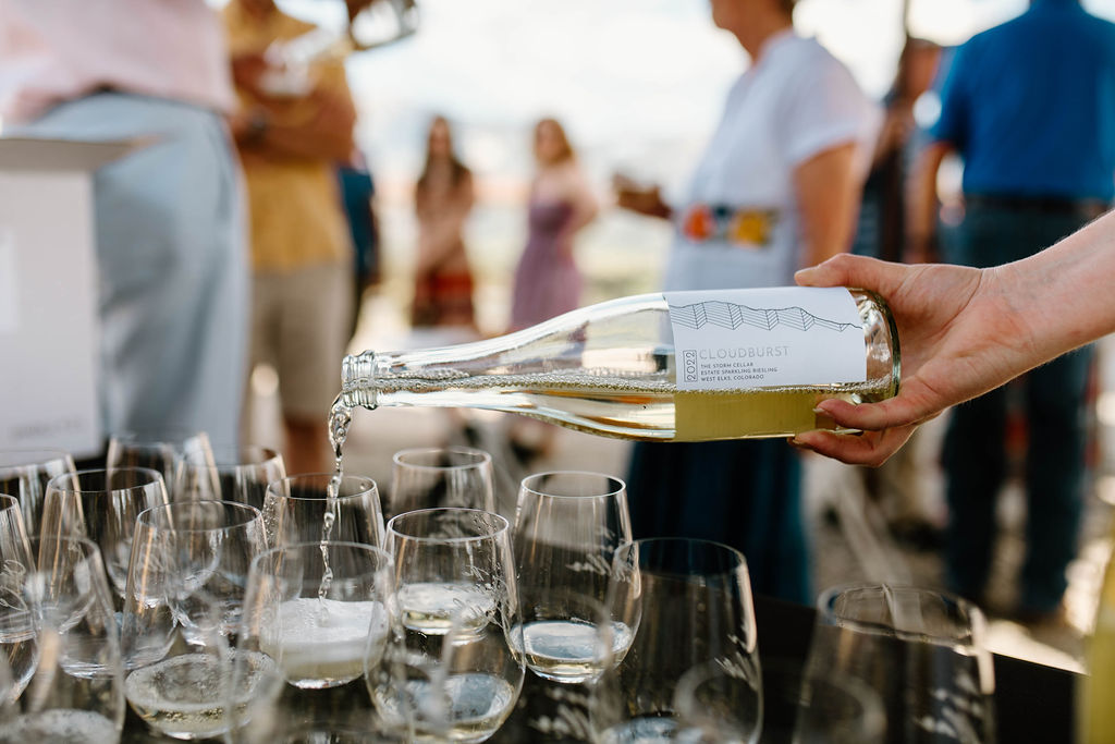 A bottle of Cloudburst sparkling Riesling being poured into empty glasses at an outdoor wine dinner.